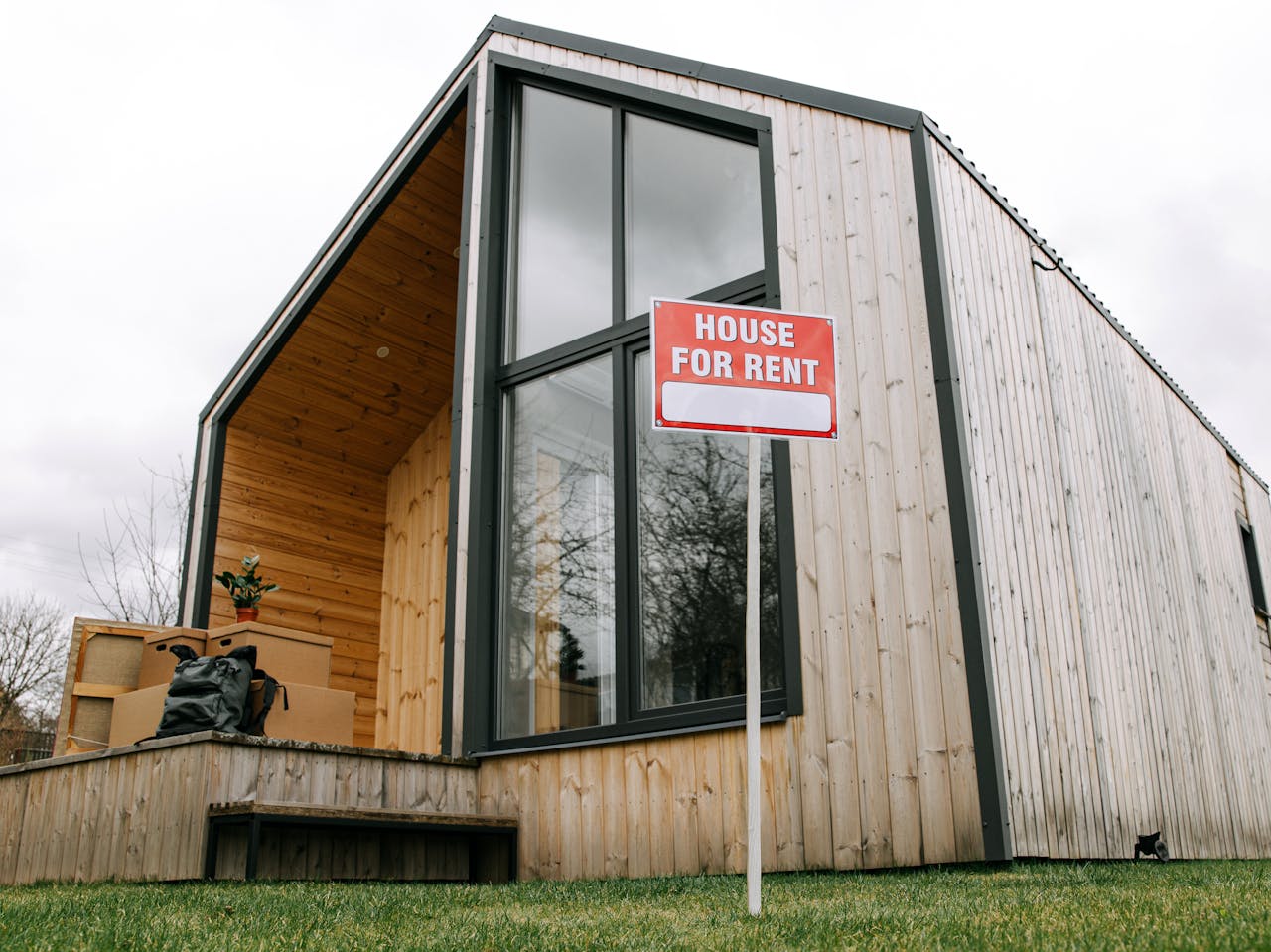 Low-angle view of a modern wooden house with a House for Rent sign, showcasing contemporary architecture.